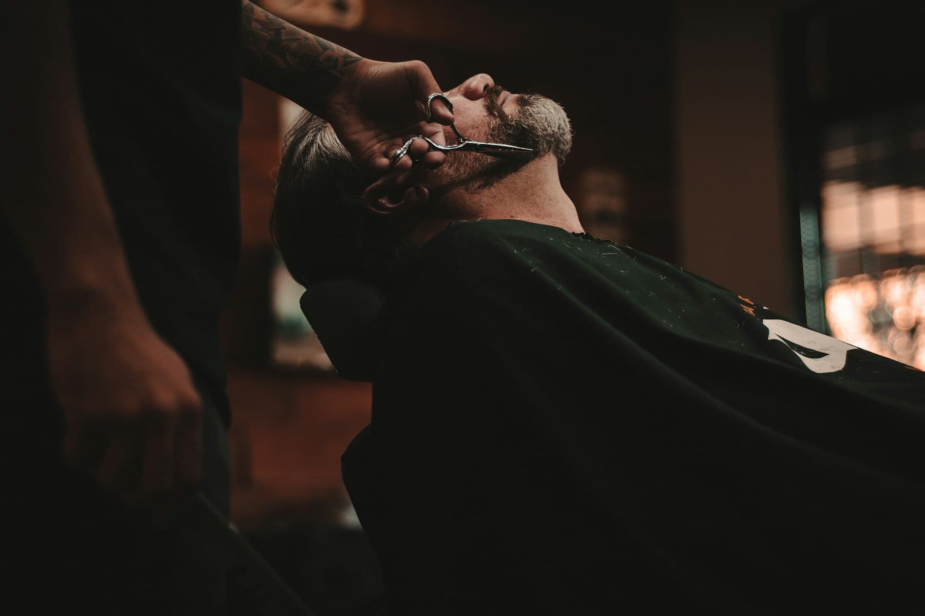 Barbero perfilando la barba de un cliente recostado en el sillón